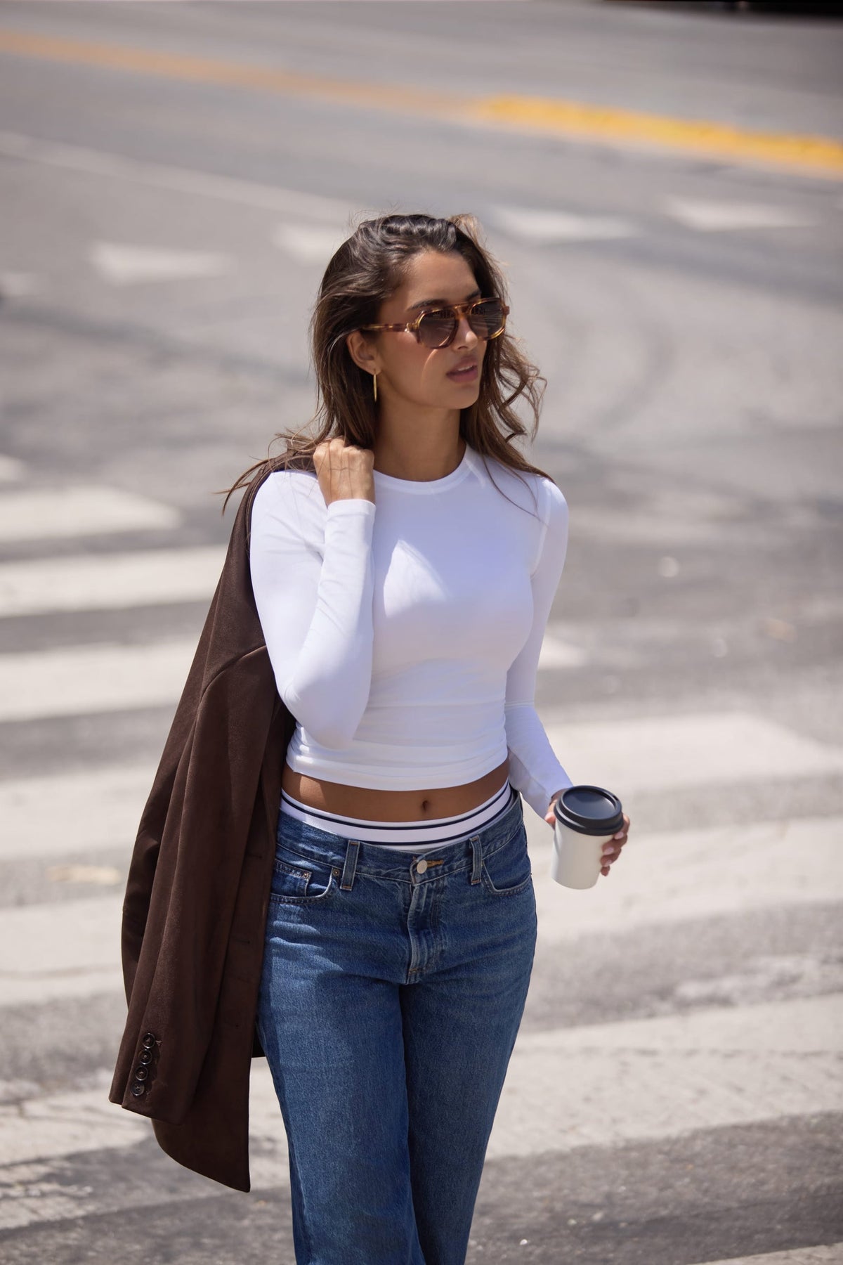 On a city street, Laura wears the Bliss Long-Sleeve Tee in White with the Bliss French-Cut Brief in Beige layered under blue jeans, carrying a coffee cup and brown coat. sizing: Kushi wears size Small