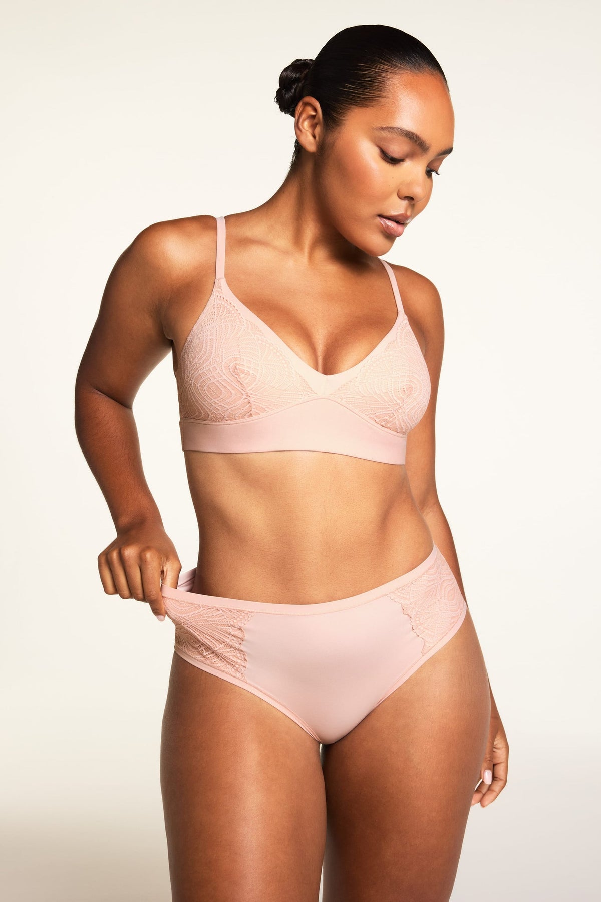 On a light studio backdrop, Amber wears the Bliss Lace Bralette and Bliss Lace Highwaist Brief in Ember Rose, showing the bralette’s thin straps and lace-trimmed V-neck alongside the high-waisted brief.