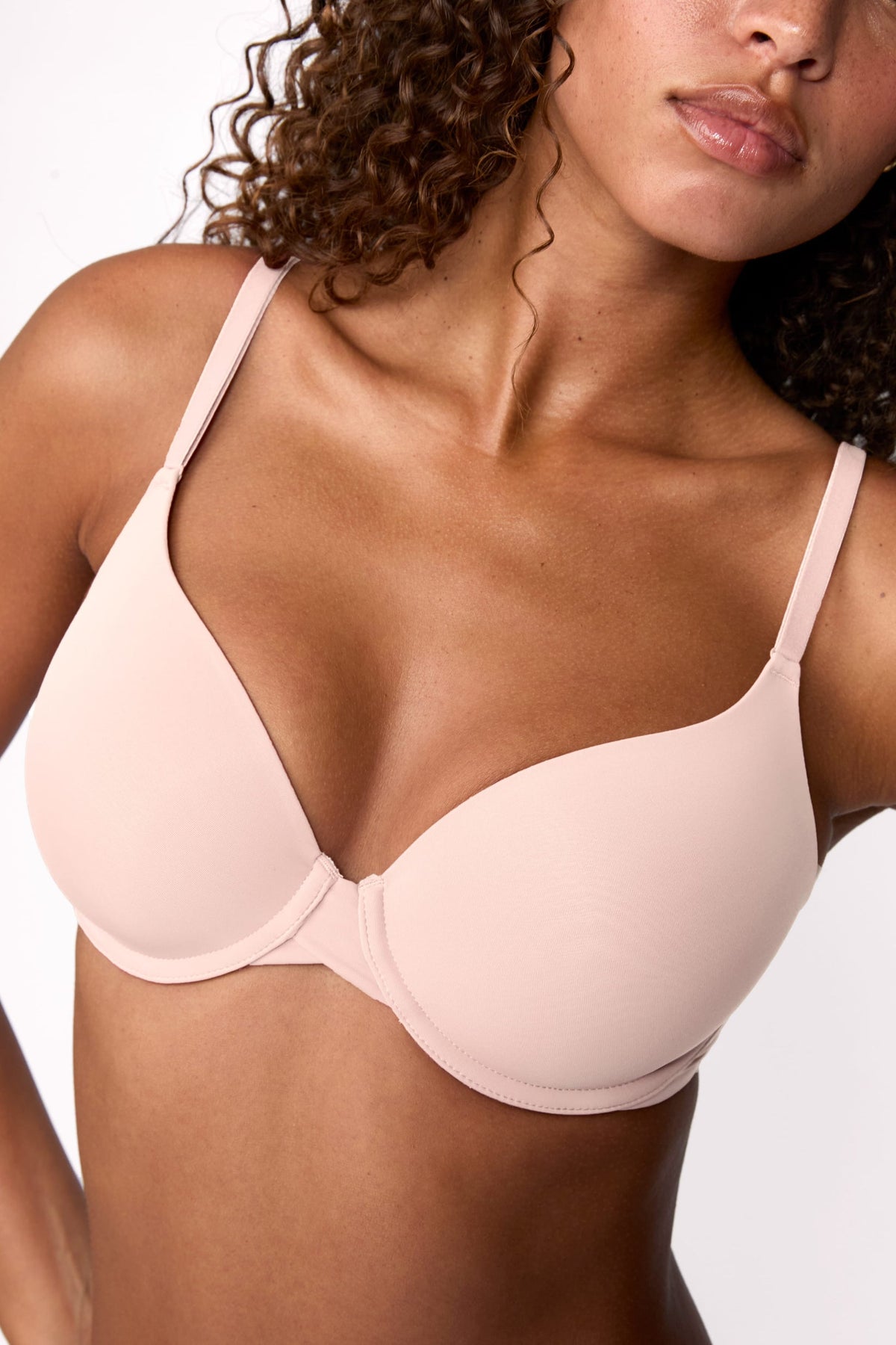 On a light studio backdrop, Courtney wears the Base T-Shirt Bra in Rose, shown in a close-up. The bra features smooth molded cups, a lightly lined design, adjustable straps, and an underwire for support. sizing: Courtney wears size 32D