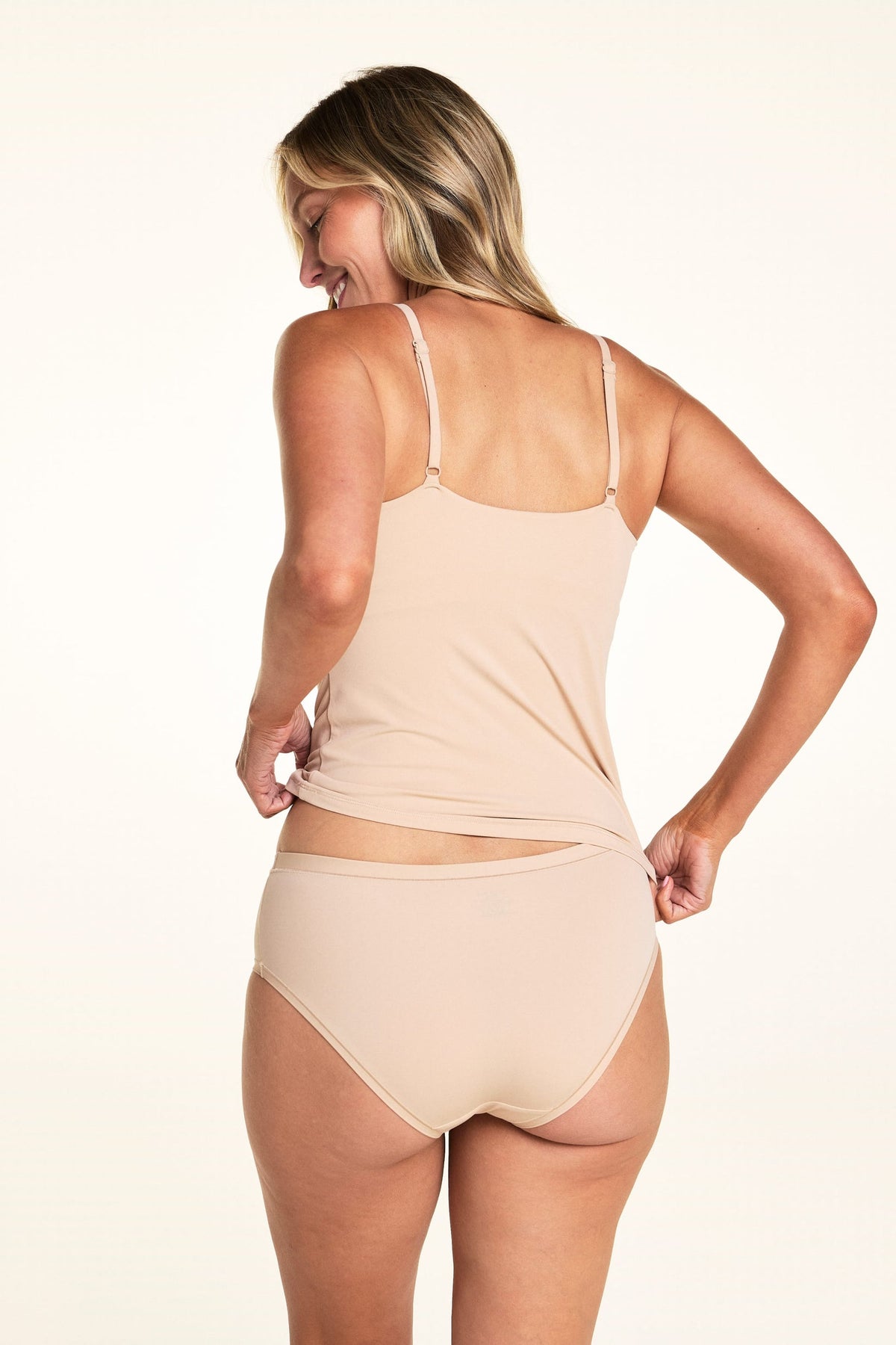 Against a white studio backdrop, Meagan faces away wearing the Bliss Cami in Beige with matching underwear, showing the straight back neckline, adjustable straps, and smooth fitted silhouette.