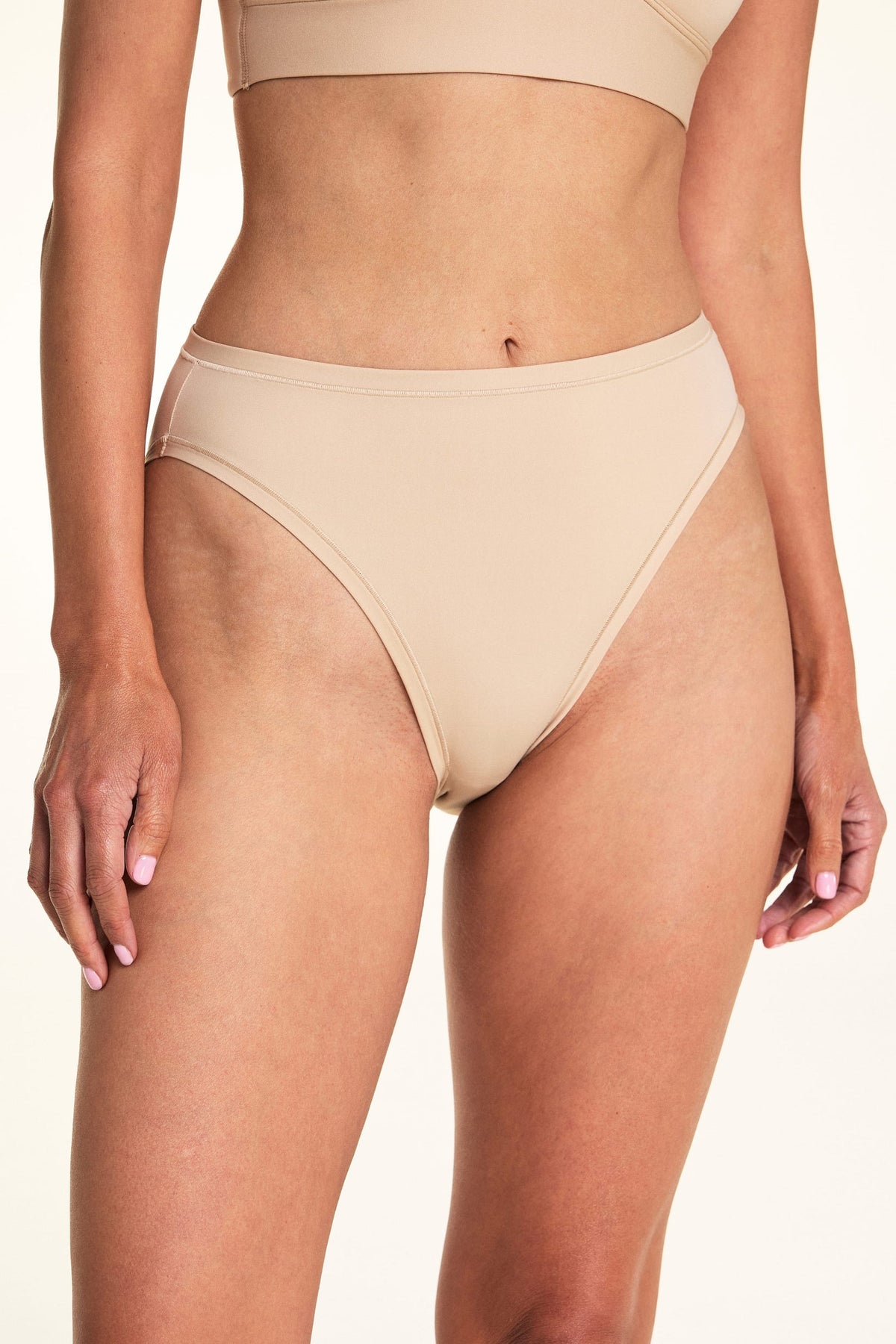 Against a white studio backdrop, Meagan wears the Bliss French Cut underwear in Beige, showing the high-rise silhouette and smooth finish in a front-facing pose.
