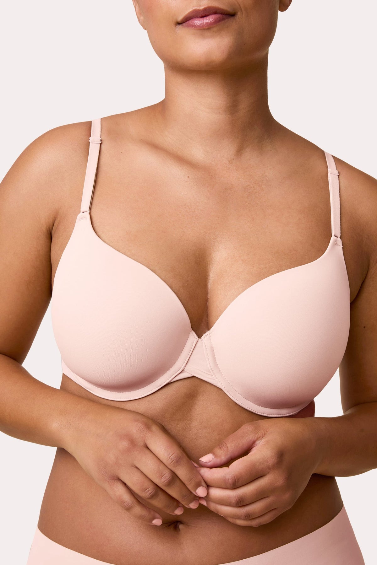 On a light studio backdrop, India wears the Base T-Shirt Bra in Rose, shown in a close-up. The bra features smooth molded cups, adjustable straps, and an underwire for support.