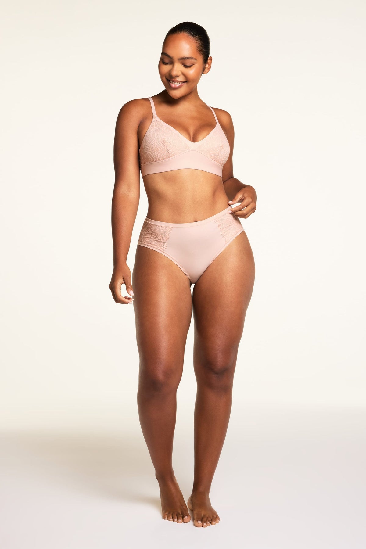 On a light studio backdrop, Amber wears the Bliss Lace Highwaist Brief in Ember Rose, shown in close-up to highlight the soft lace panels and high-waisted design.