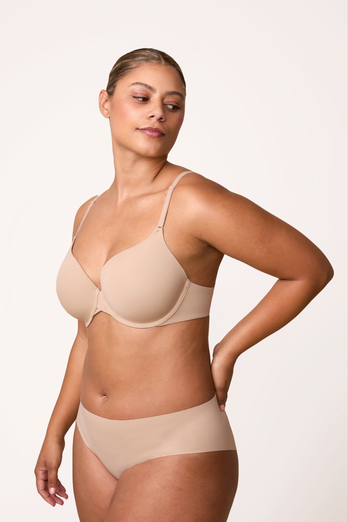 On a light neutral studio backdrop, India wears the Base T-Shirt Bra in Beige with matching underwear, shown in a side profile. The lightly lined cups provide full coverage, and the soft microfiber fabric creates a smooth, everyday silhouette. sizing: India wears size 36D