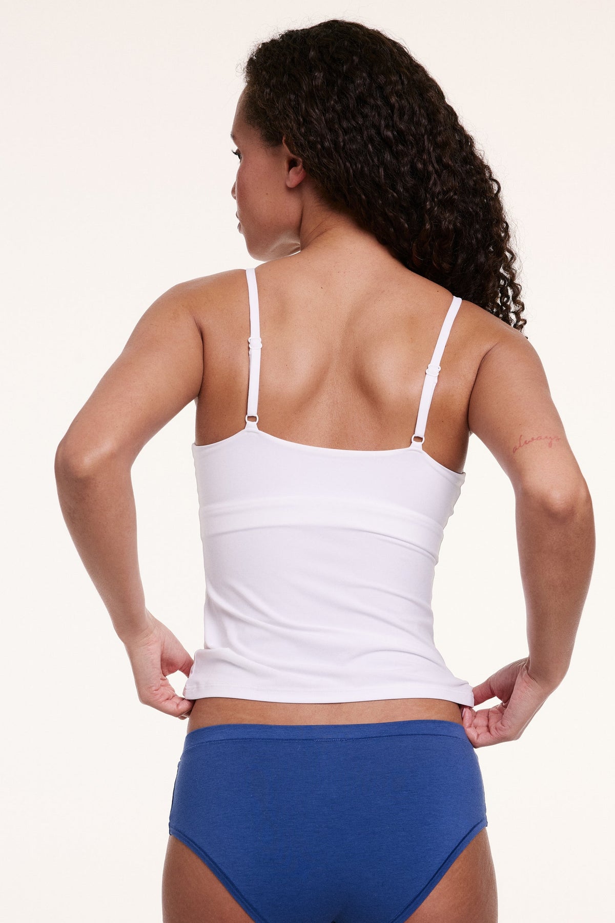 Shown from the back in a studio setting, Courtney wears the Bliss Cami in White. The thin adjustable straps and smooth, stretchy microfiber fabric create a flexible, stay-put fit.