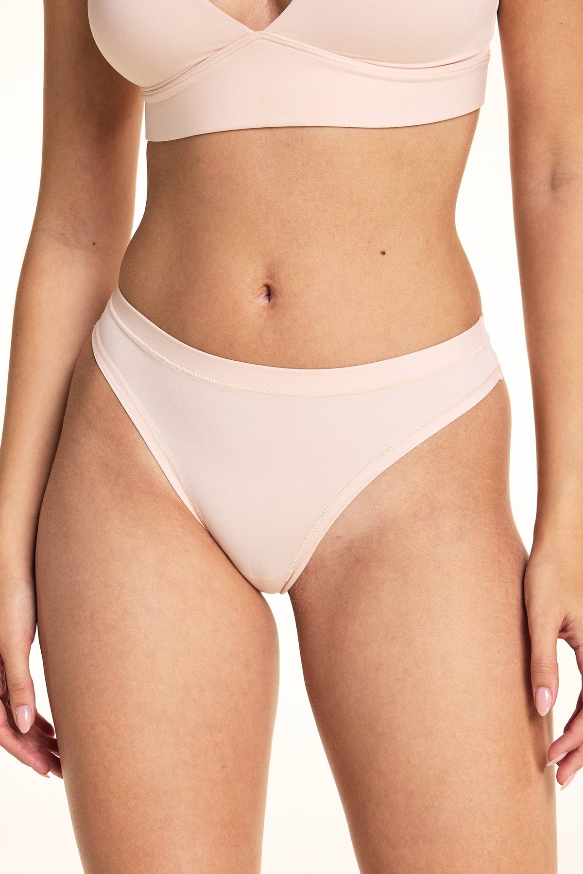 In a studio setting, Laura wears the Bliss Thong in Rose, featuring a smooth microfiber finish, low-rise silhouette, and minimal back coverage with soft elastic trim along the waistband and leg openings. sizing: Rose wears size Small