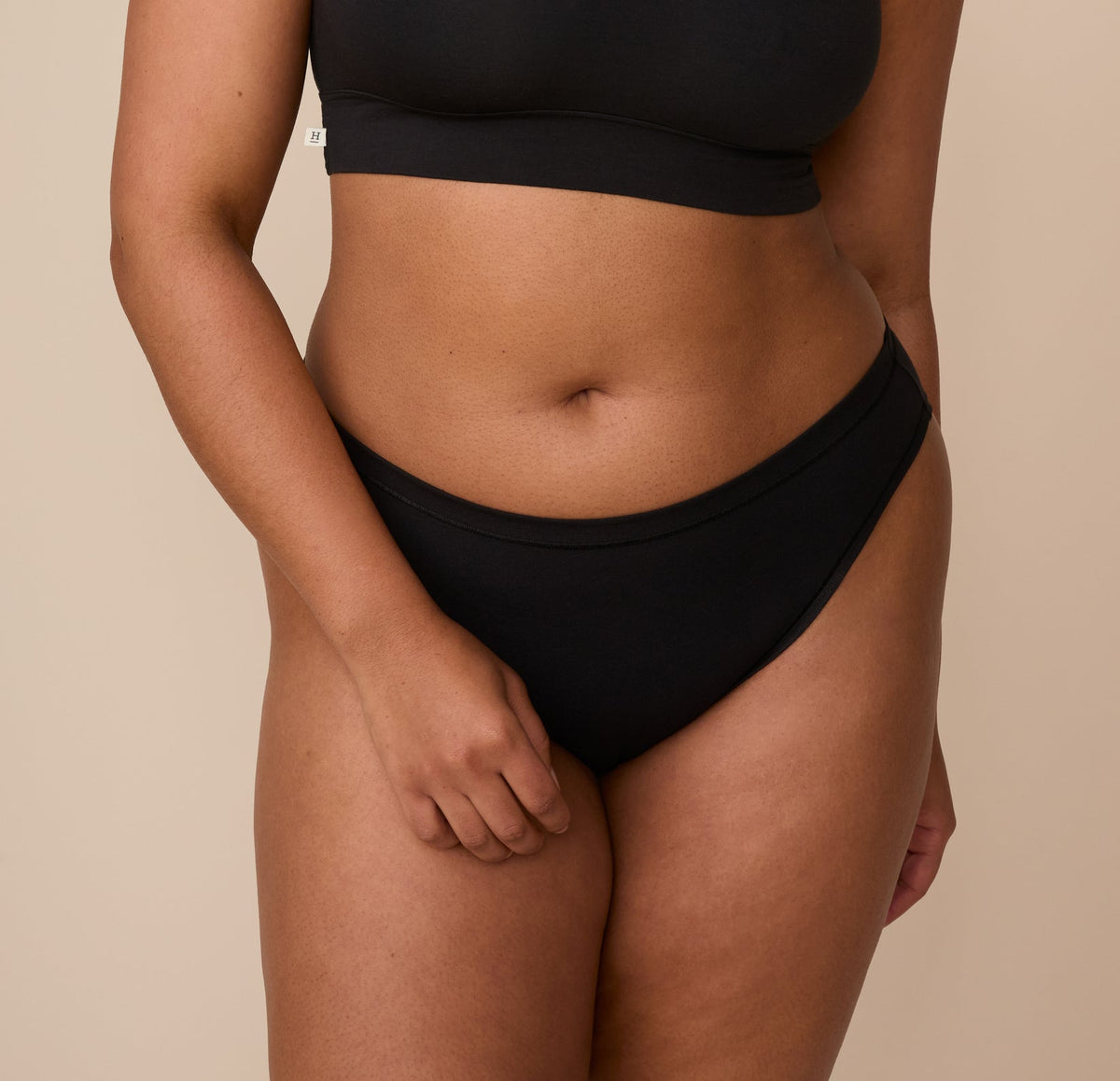 Close-up front view of Zarria wearing the Cloud Cotton Bikini in Black. The image highlights the bikini's mid-rise waistband and smooth, barely-there leg openings, showcasing the soft, breathable fabric. sizing: Zarria wears size XL