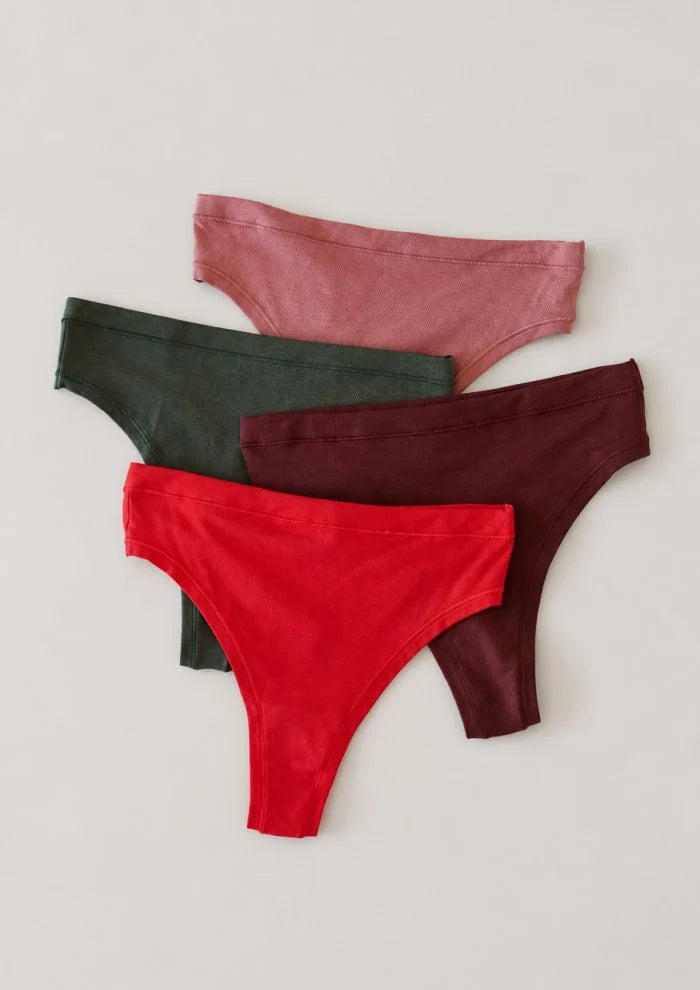 Flat lay of four ribbed knit underwear pieces in seasonal colors — pink, olive, burgundy, and red.